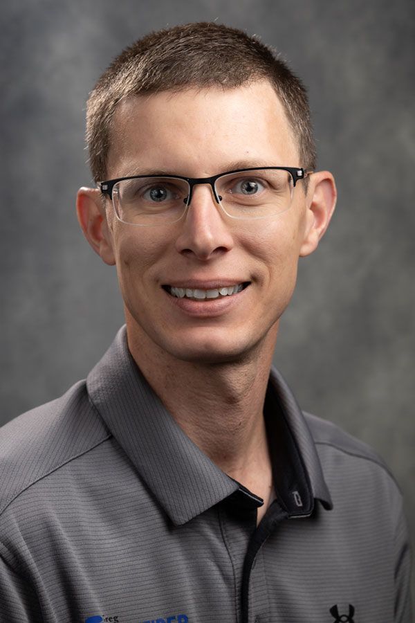 A man wearing glasses and a gray shirt is smiling for the camera.