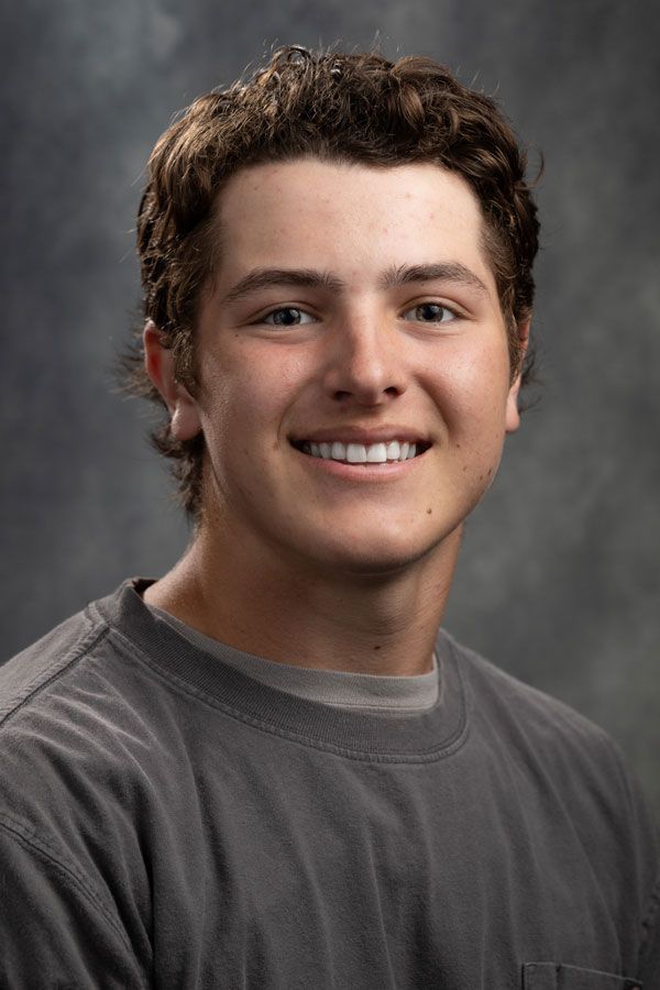 A young man in a gray shirt is smiling for the camera.
