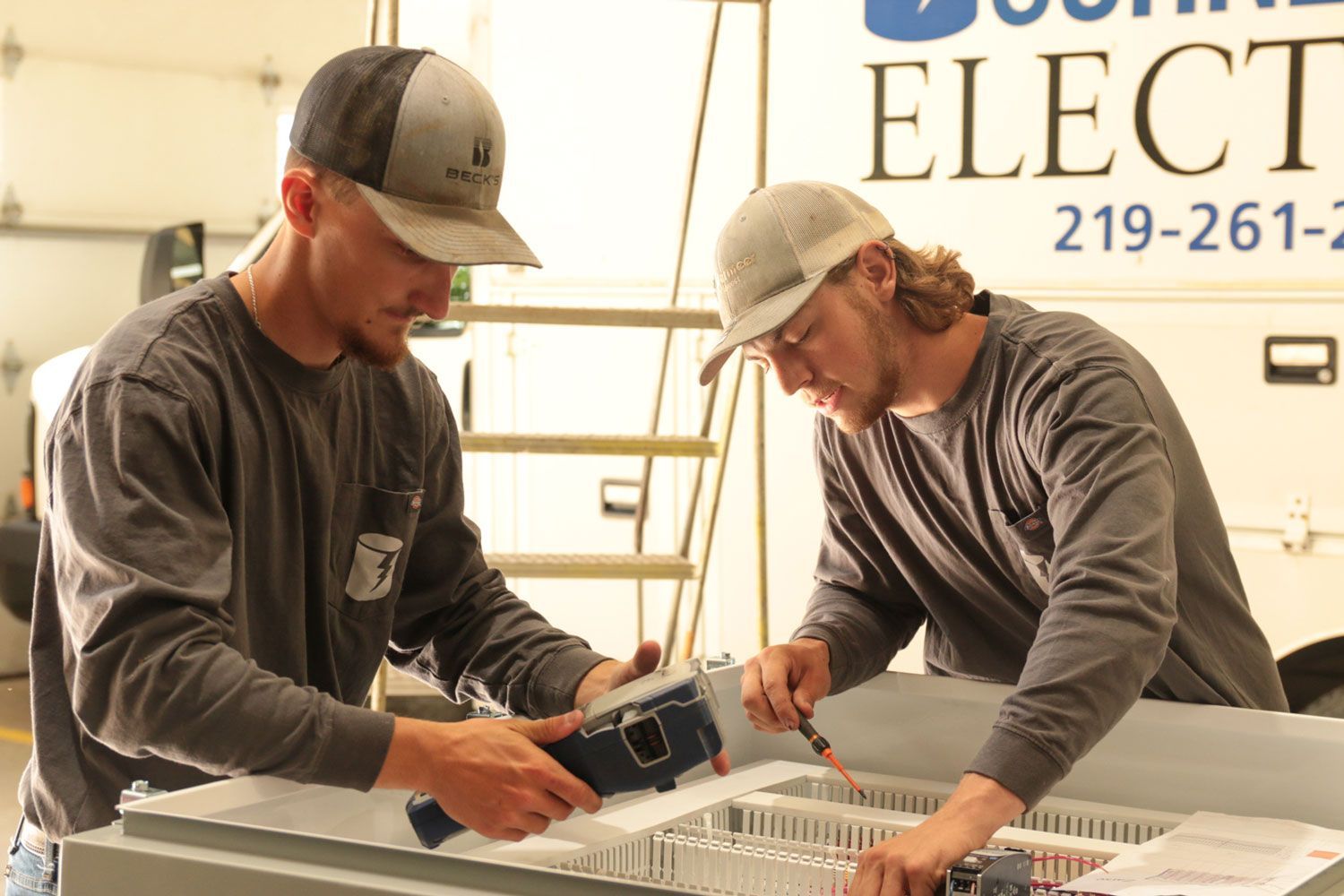 Two men are working on a piece of equipment in front of a sign that says elec