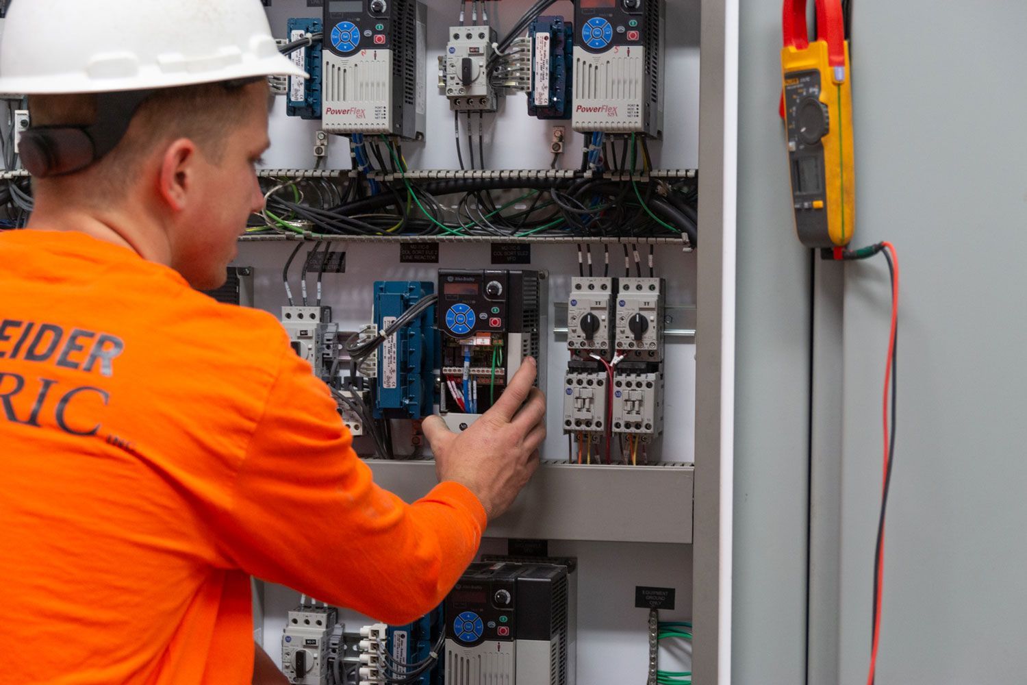 A man in an orange shirt is working on an electrical box.