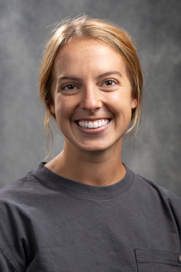 A woman in a gray shirt is smiling for the camera.