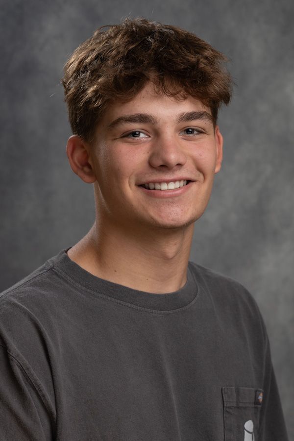 A young man in a gray shirt is smiling for the camera.