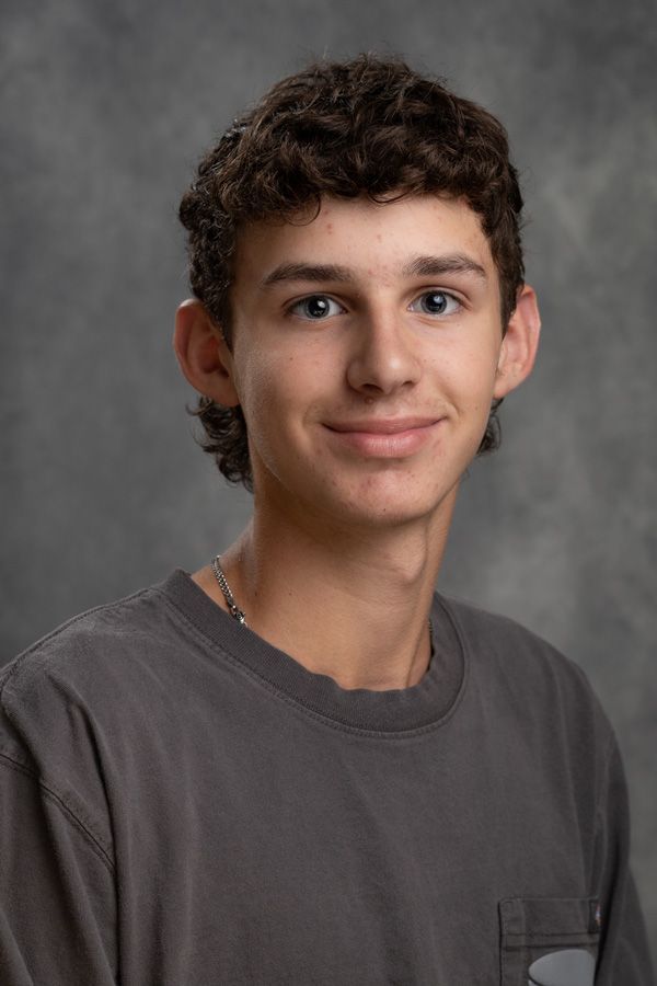 A young man with curly hair is wearing a gray shirt and smiling for the camera.