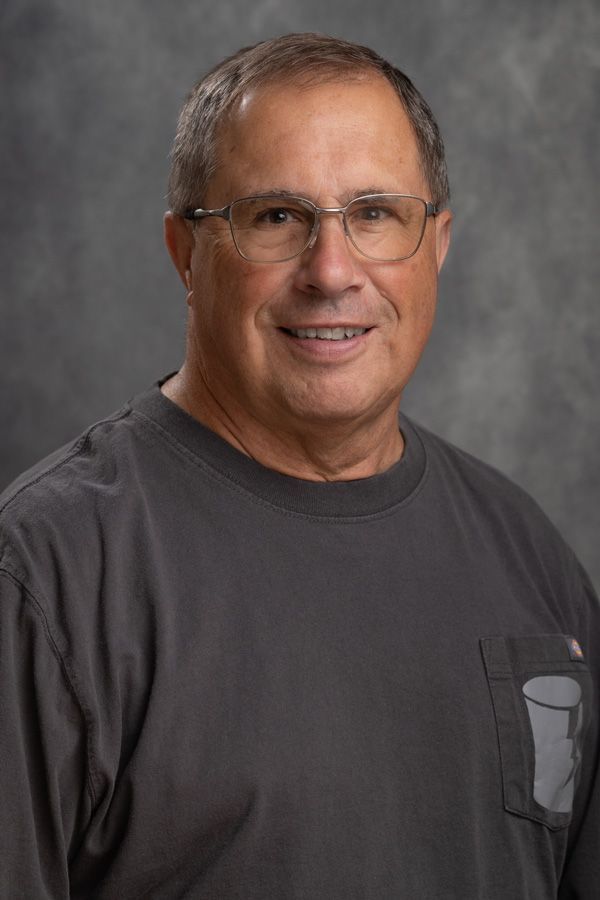 A man wearing glasses and a gray shirt is smiling for the camera.