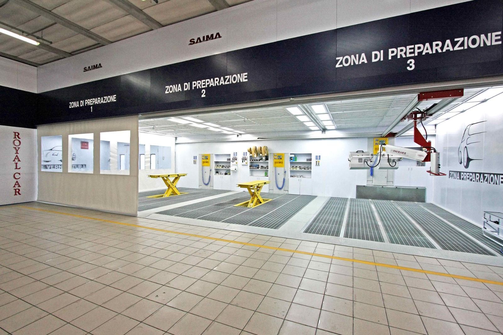 Cabina di verniciatura per auto moderna con pavimento piastrellato, supporti gialli e attrezzature aeree in un'officina pulita.