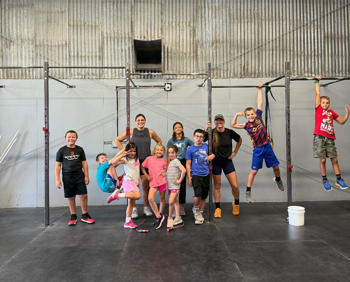 Group of children smiling in the gym at Hangar CrossFit in Spanish Fork, UT with pull-up bars.