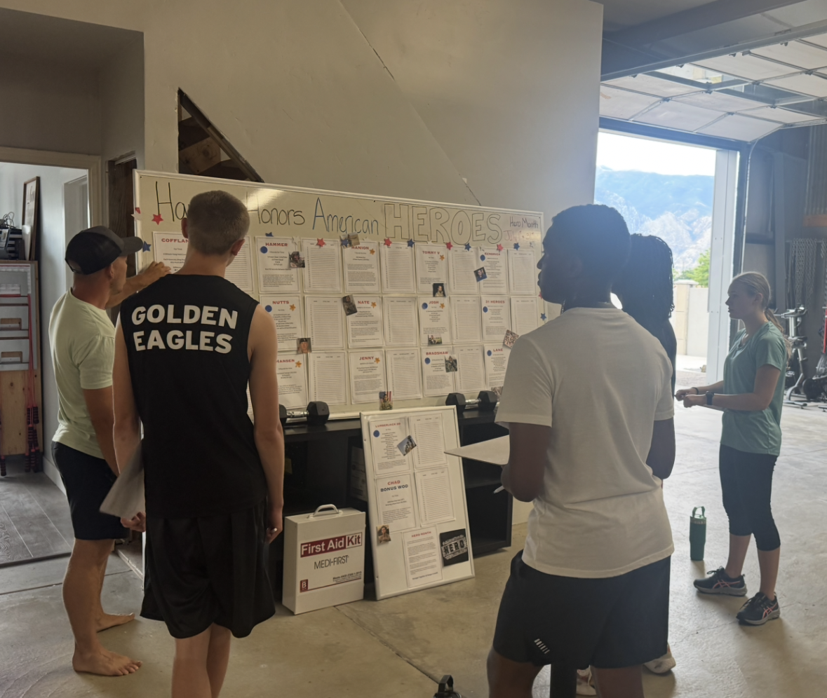 Group of people looking at a whiteboard with papers posted on it indoors; mountains visible through an open doorway.