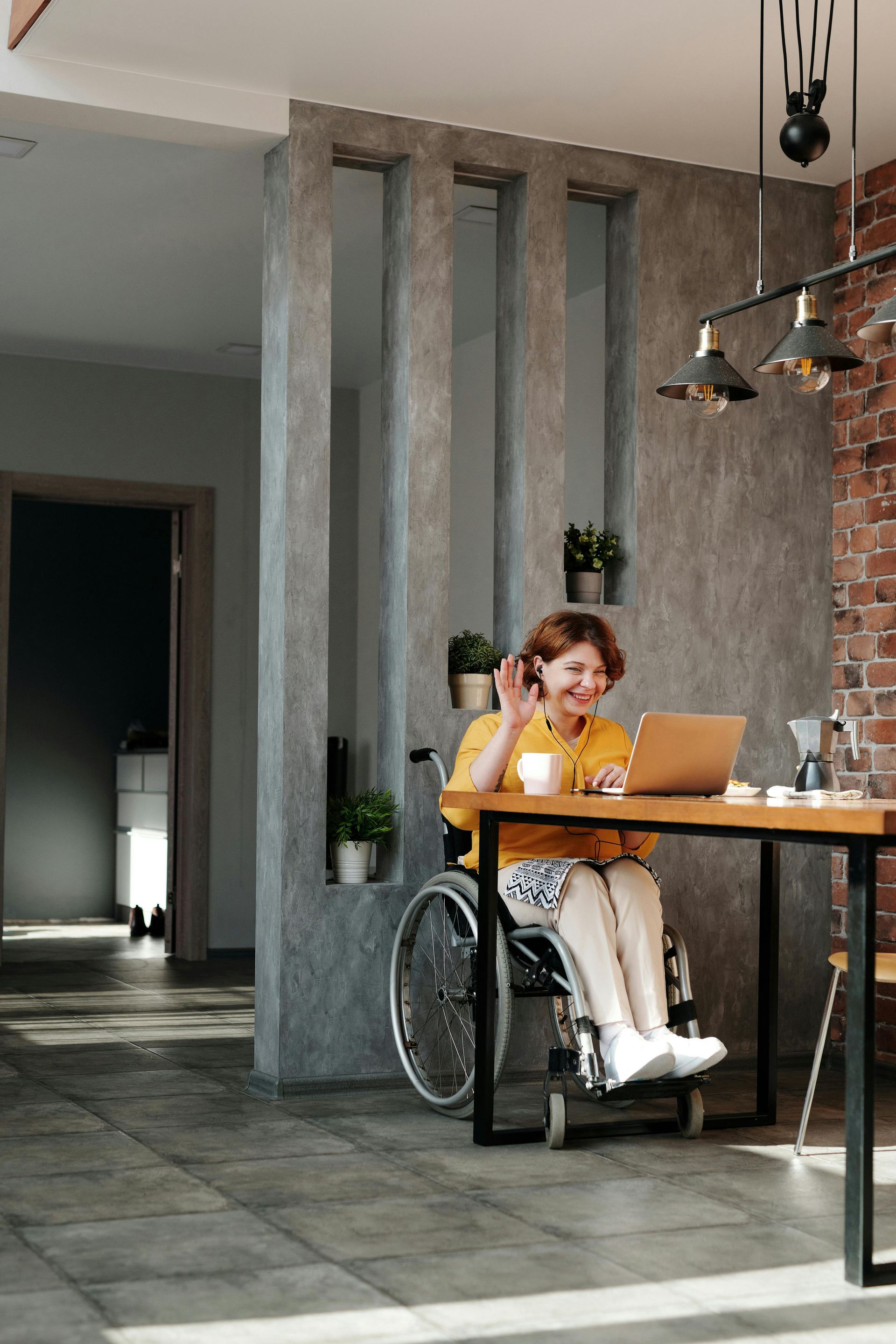 A woman in a wheelchair is sitting at a table using a laptop computer.