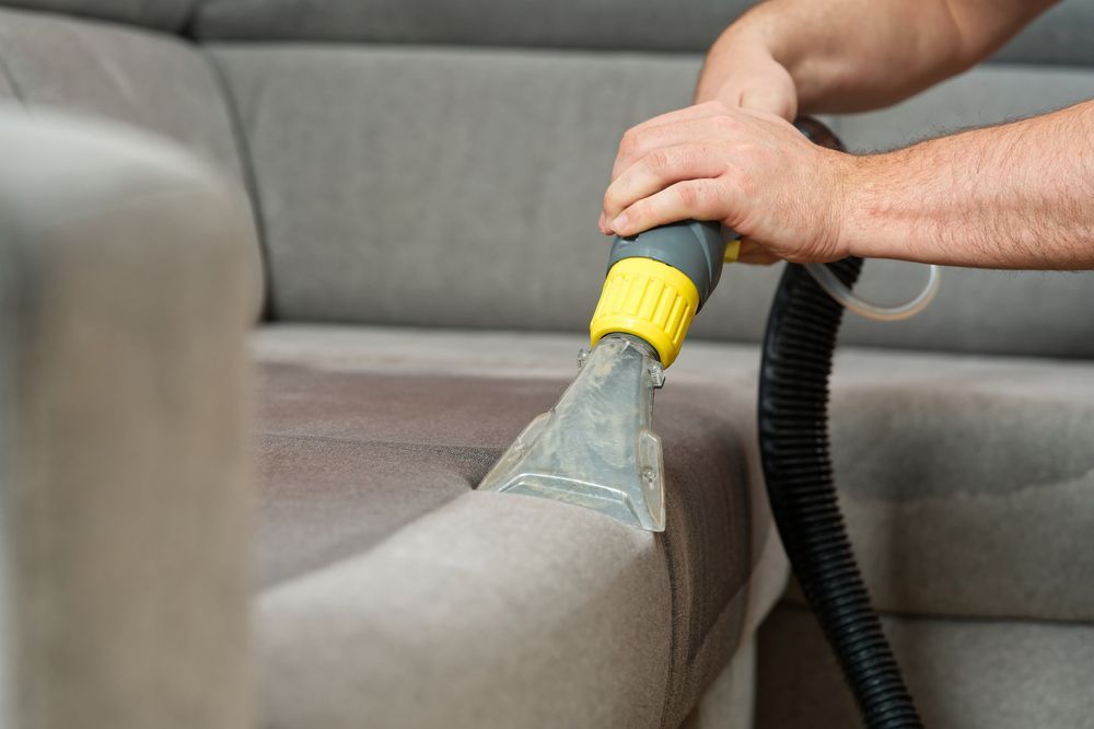 A Man Is Cleaning A Couch With A Vacuum Cleaner — Mr Steam Clean Tweed Coast In Kingscliff, NSW