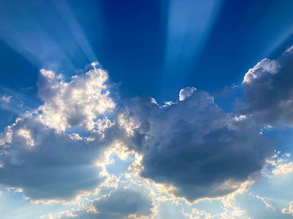Crepuscular rays beaming from behind clouds, against a deep blue sky backdrop
