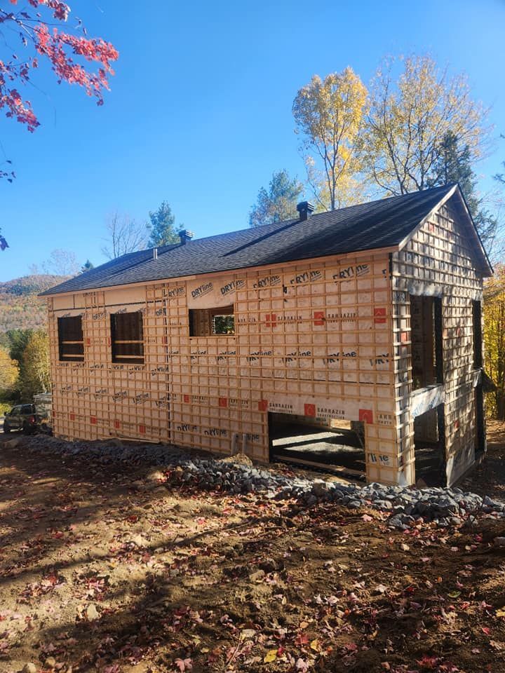 Bâtiment en construction avec bardage en bois, toit sombre et portes ouvertes.