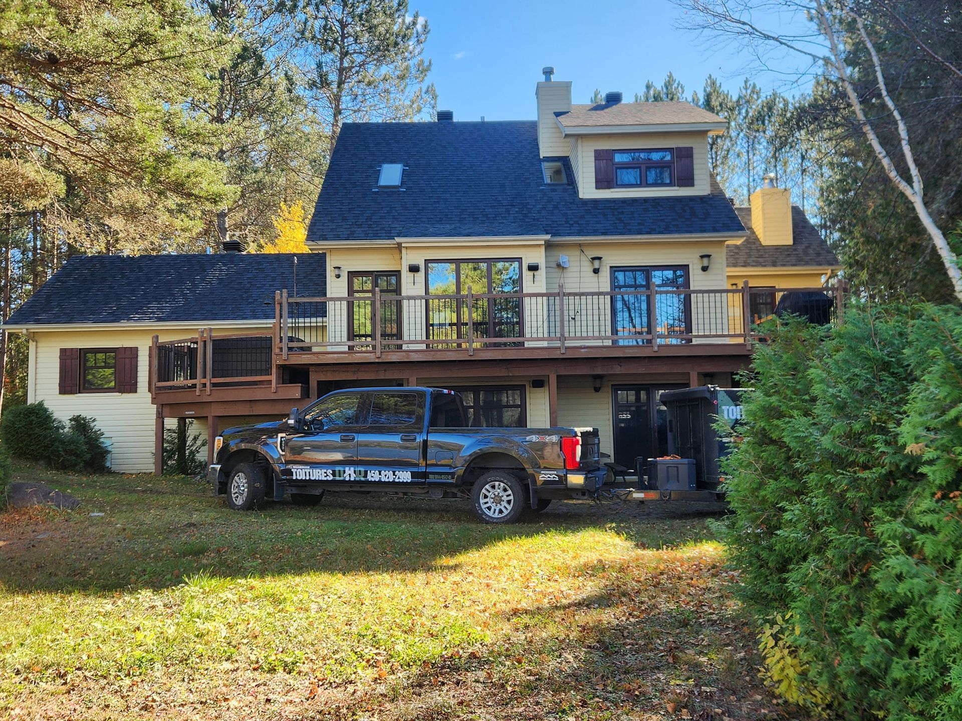 Maison beige avec toit noir et terrasse en bois. Un camion est garé devant.