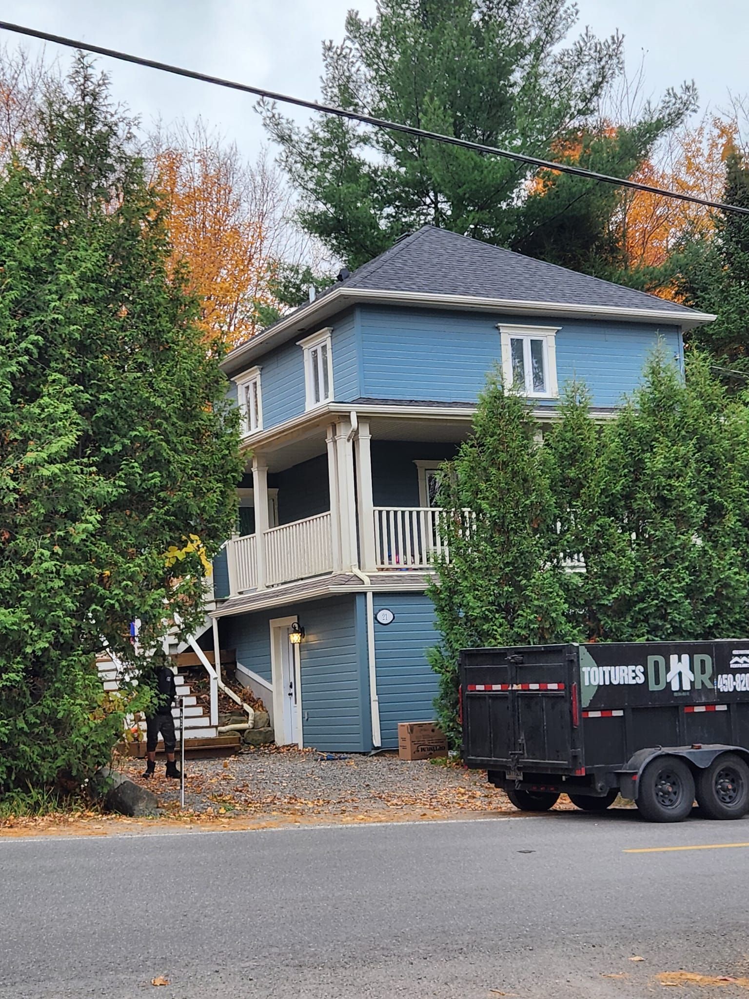 Maison bleue à deux étages avec des boiseries blanches ; une caravane est garée à proximité.