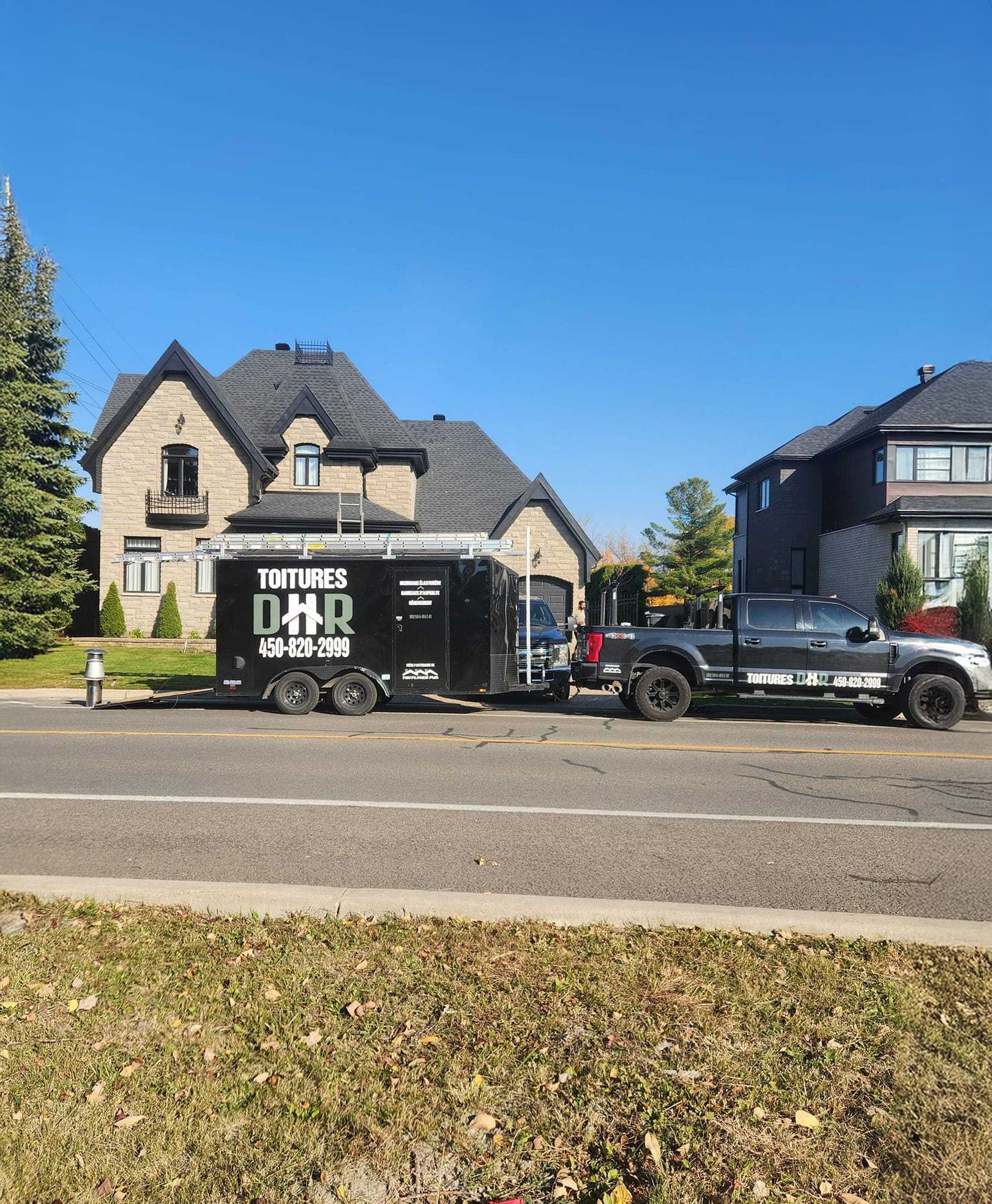 Un camion noir tractant une remorque est stationné devant une maison par une journée ensoleillée.