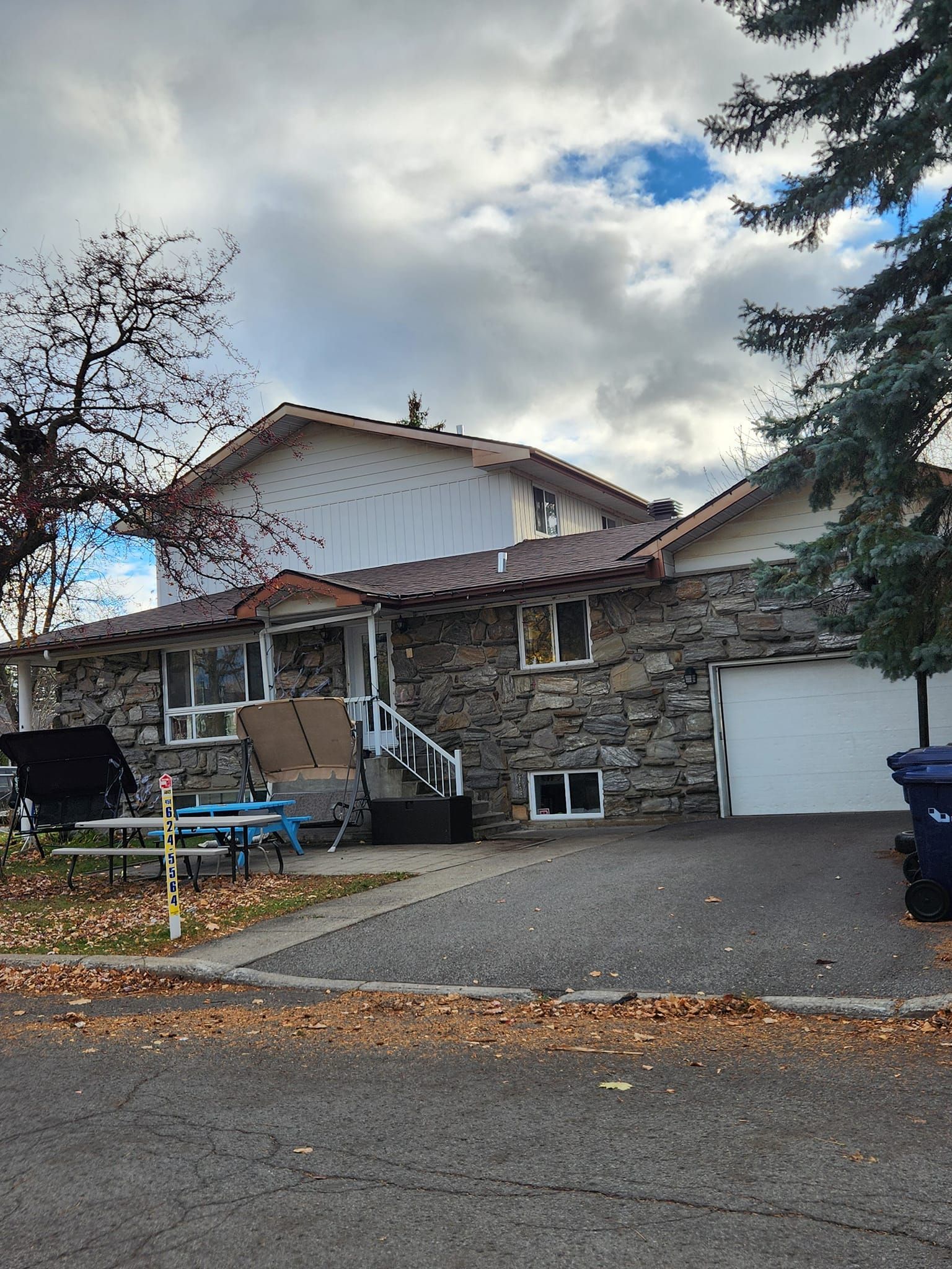 Maison en pierre avec porte de garage blanche et porche, se détachant sur un ciel nuageux.