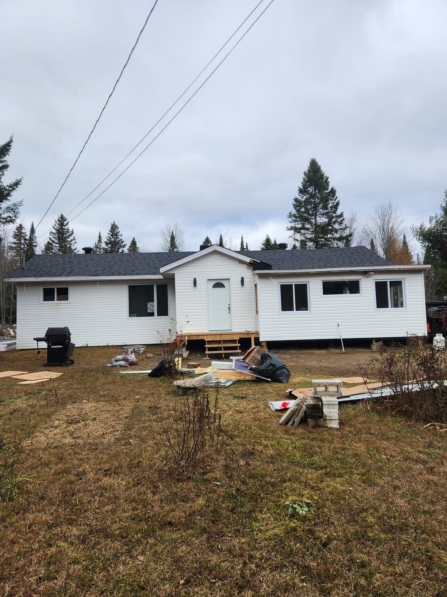 Maison blanche avec un nouveau revêtement extérieur ; ouvrier à l'extérieur ; bardeaux de toiture ; journée nuageuse.