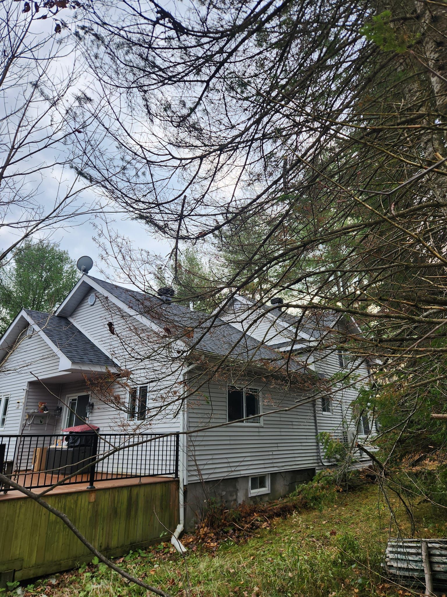 Maison blanche avec terrasse masquée par des branches d'arbres sous un ciel nuageux.