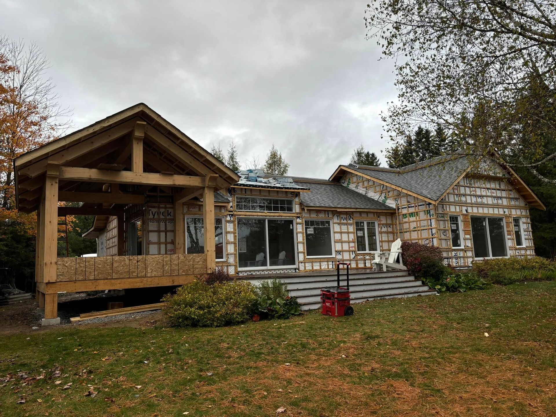 Maison en rénovation avec charpente apparente et nouvelle véranda couverte. Ciel couvert et feuillage d'automne.