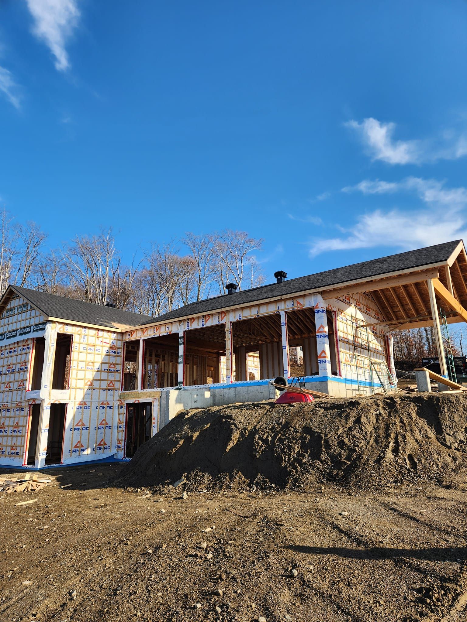 Chantier de construction d'une maison sous un ciel bleu, charpente en bois visible sous sa bâche de protection.