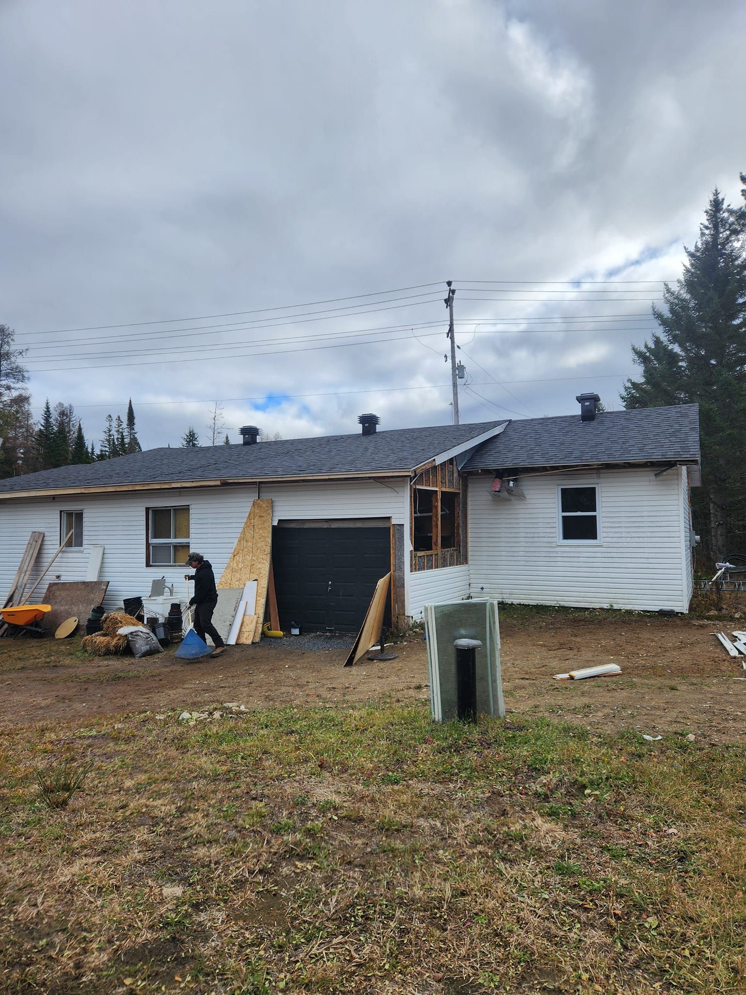 Maison en construction, une personne se tient à proximité ; ciel nuageux.