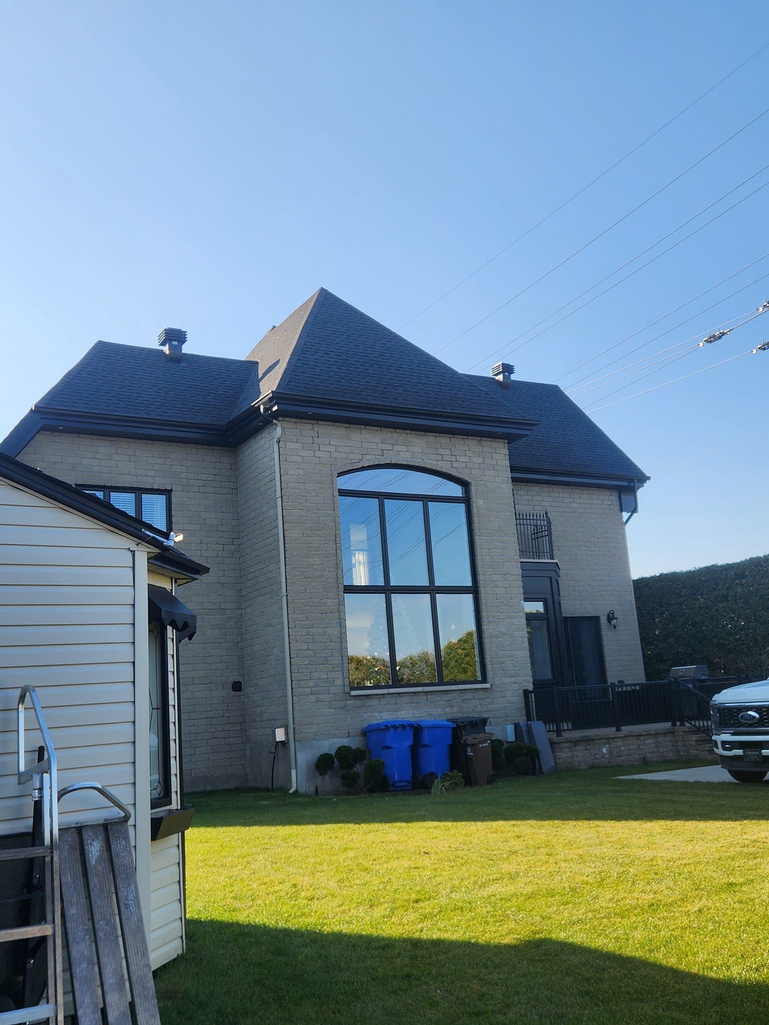 Maison en briques de deux étages avec un toit sombre et une grande fenêtre cintrée ; ciel bleu et herbe verte.