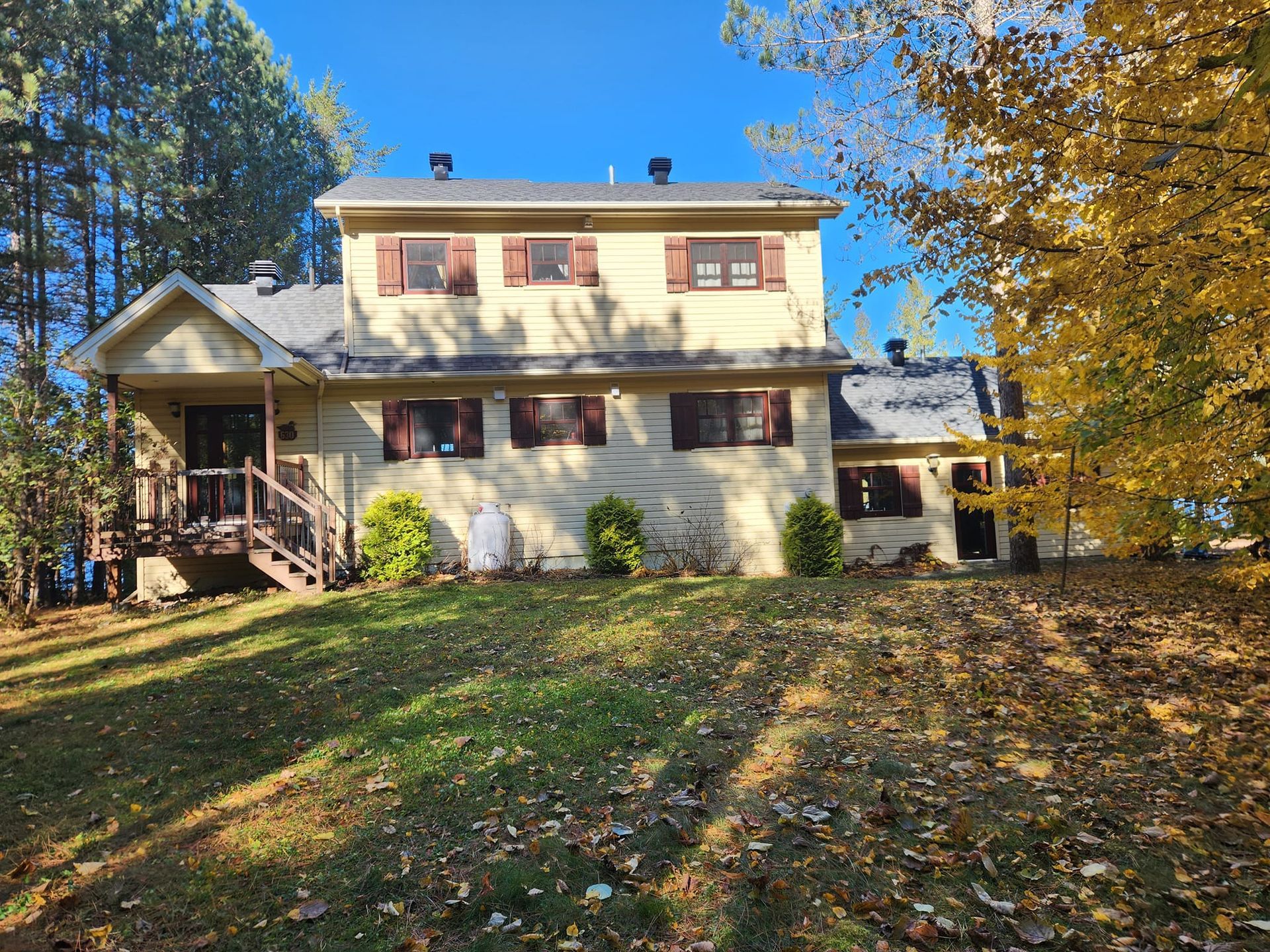 Maison jaune à deux étages avec des volets bruns, située sur une colline herbeuse. 