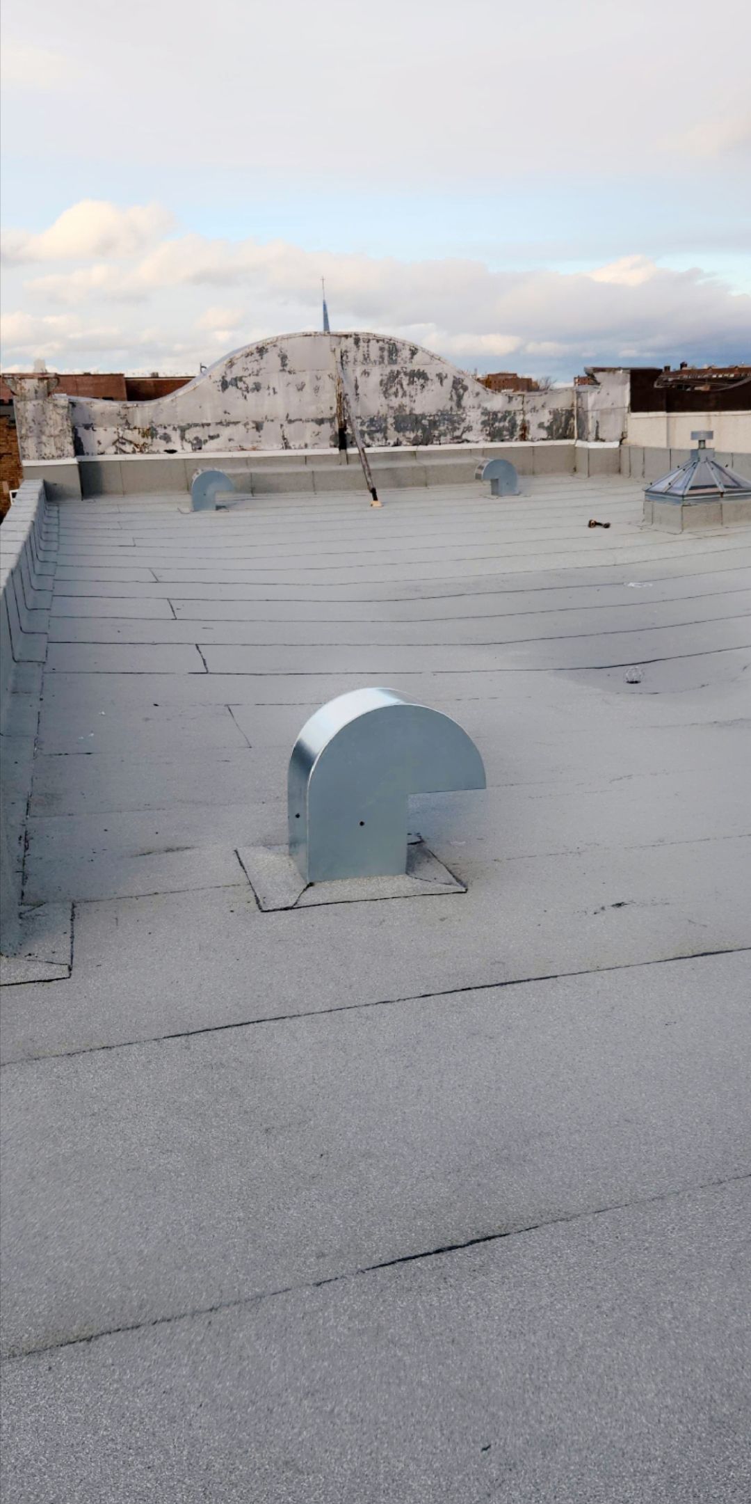 Un toit plat équipé d'un système de ventilation, un autre bâtiment en arrière-plan et un ciel nuageux.