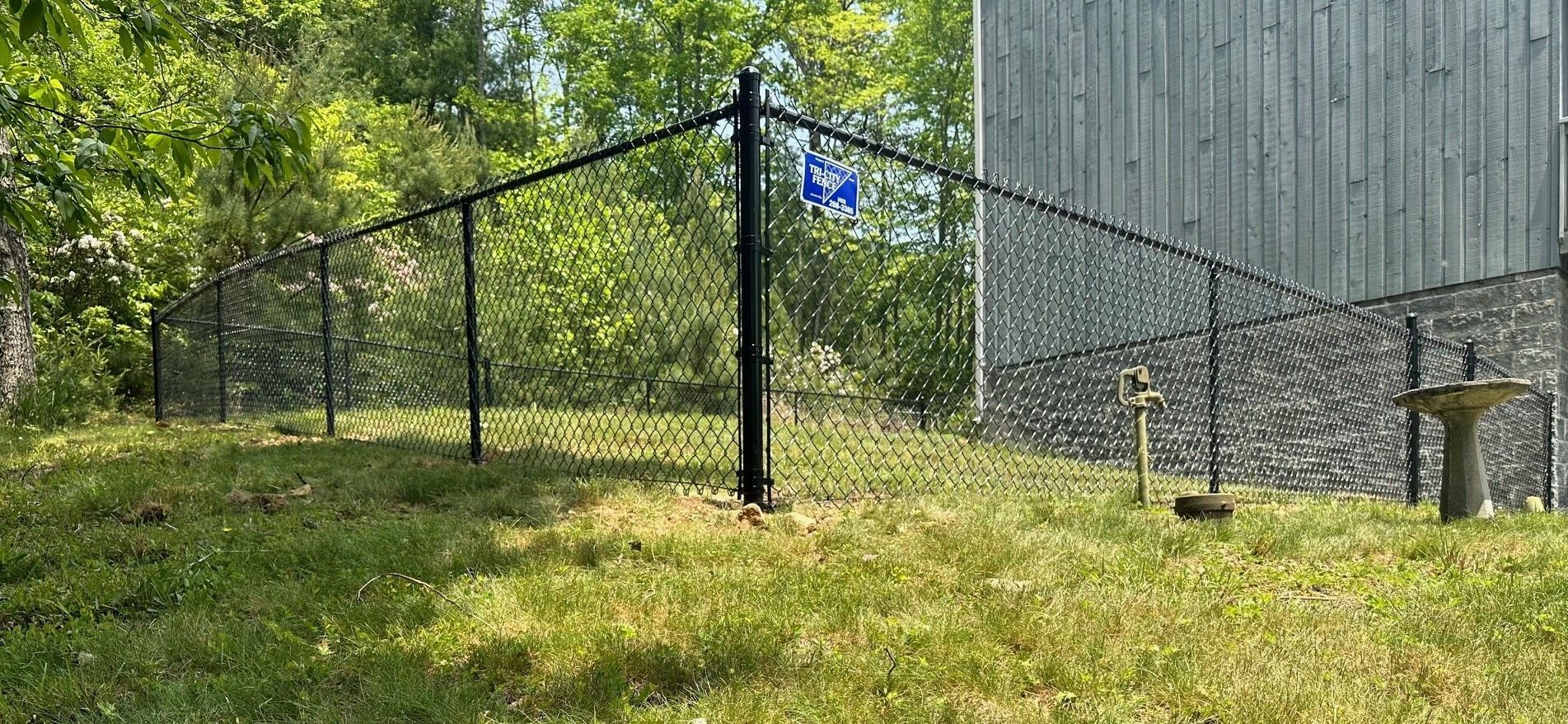 A chain link fence is in the grass in front of a building.