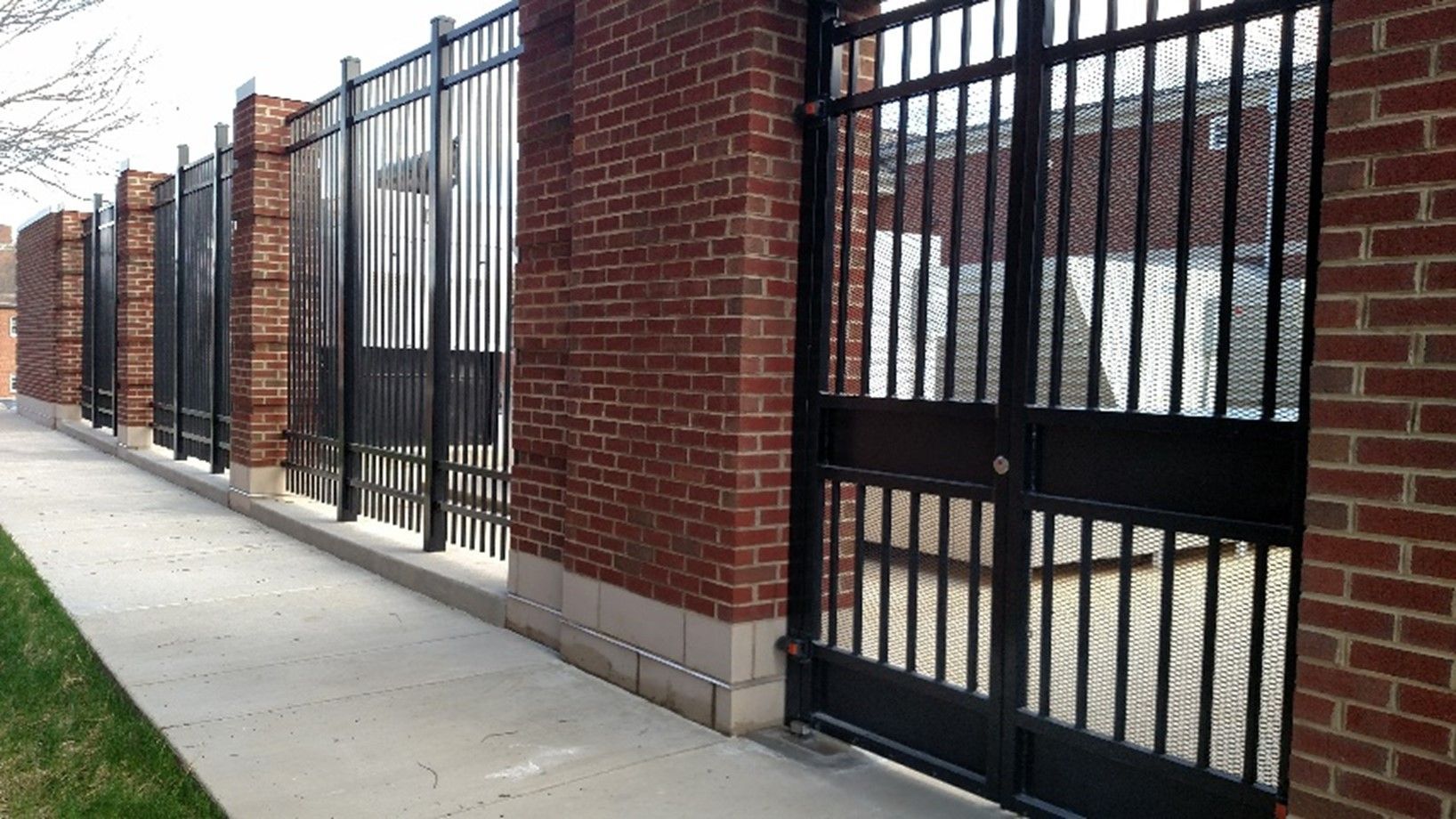 A secure metal fence with brick columns outside a modern commercial building.