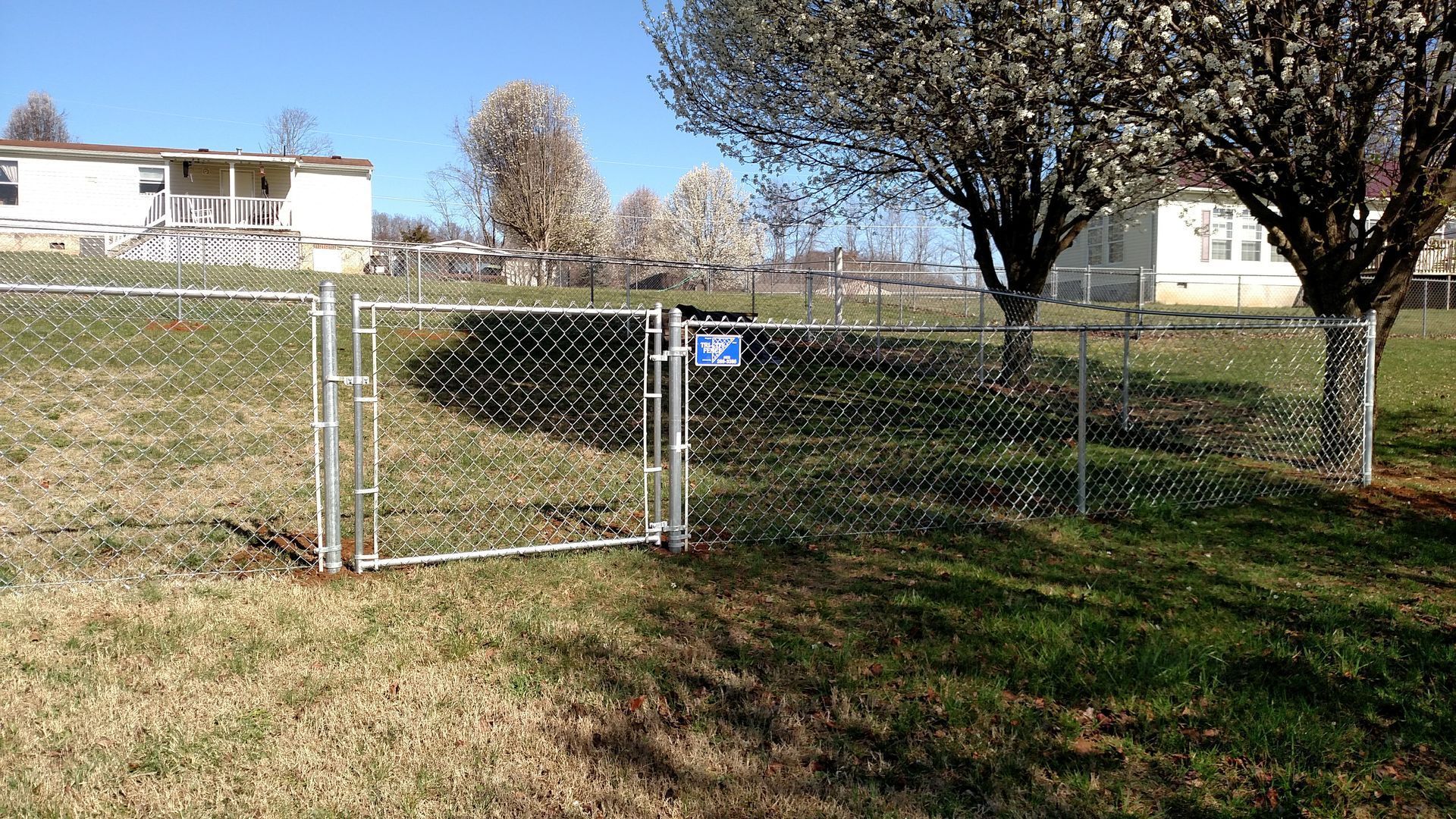A chain link fence with a gate in the middle of a grassy field.