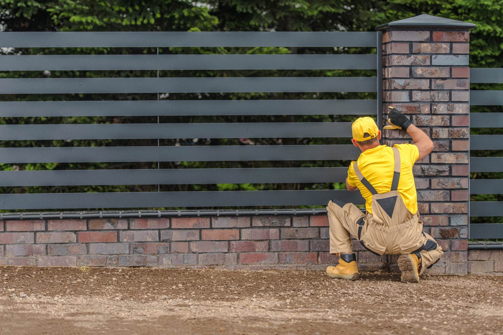A local fence contractor wearing a yellow uniform, installing residential metal panels on a fence.