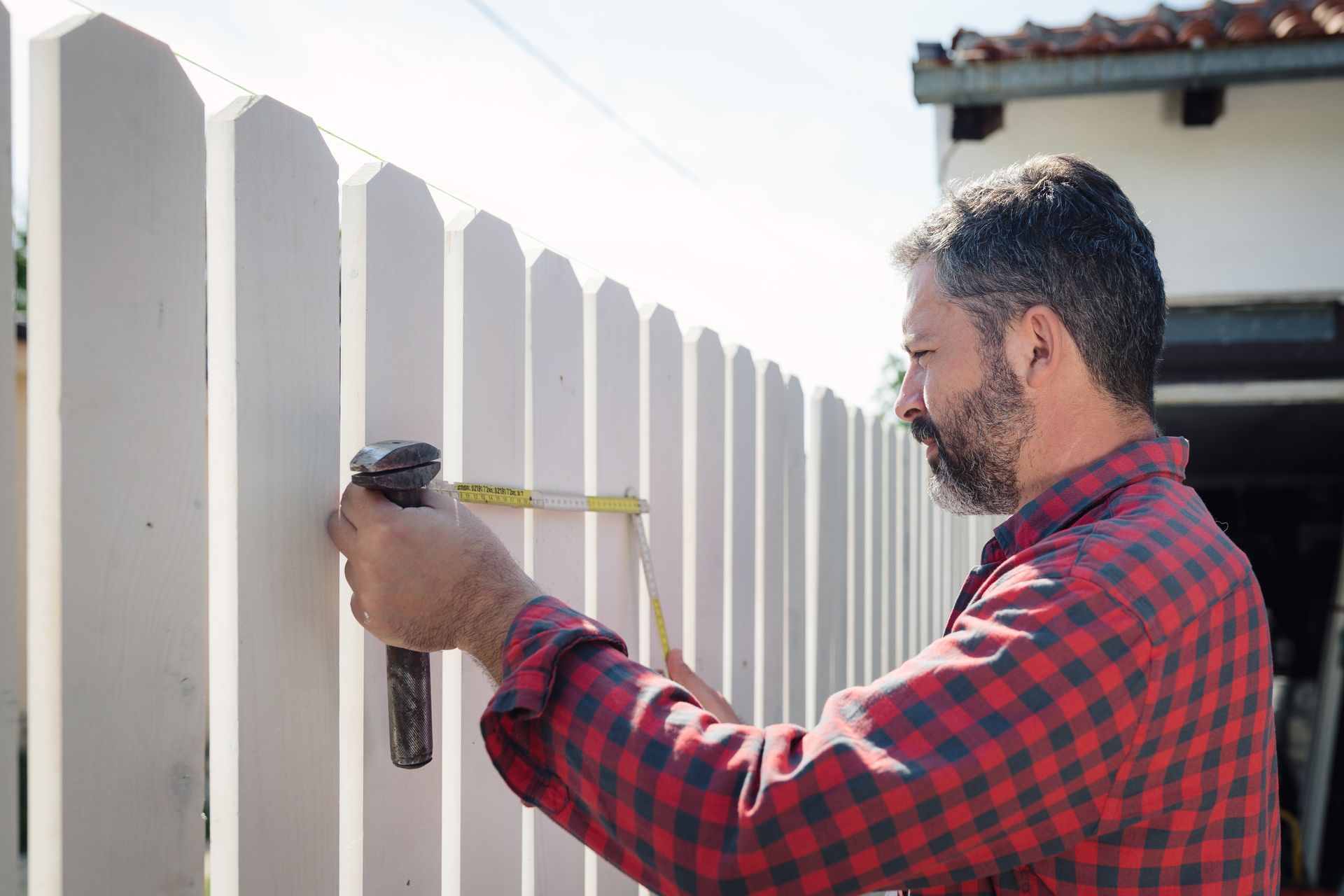 A man measuring a white fence with a tape measure, showcasing a professional local fence company.