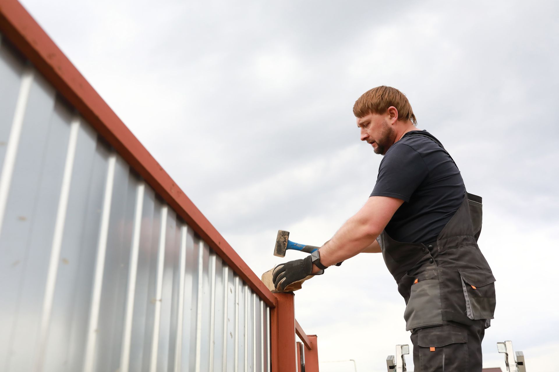 A man in overalls constructs a fence with a hammer, representing Tri-City Fence Company.