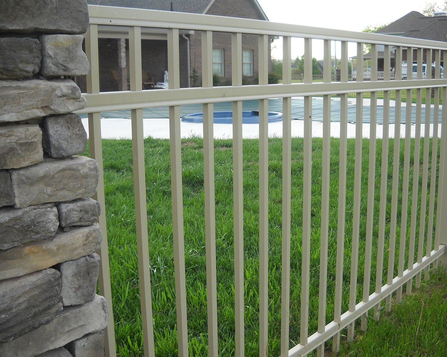 A metal fence surrounds a lush green yard with a pool in the background