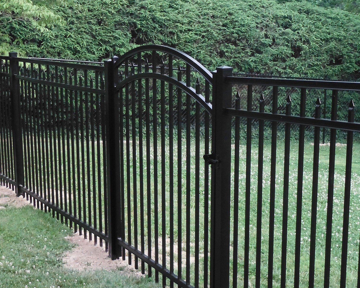 A black wrought iron fence with a gate in the middle of a lush green field.