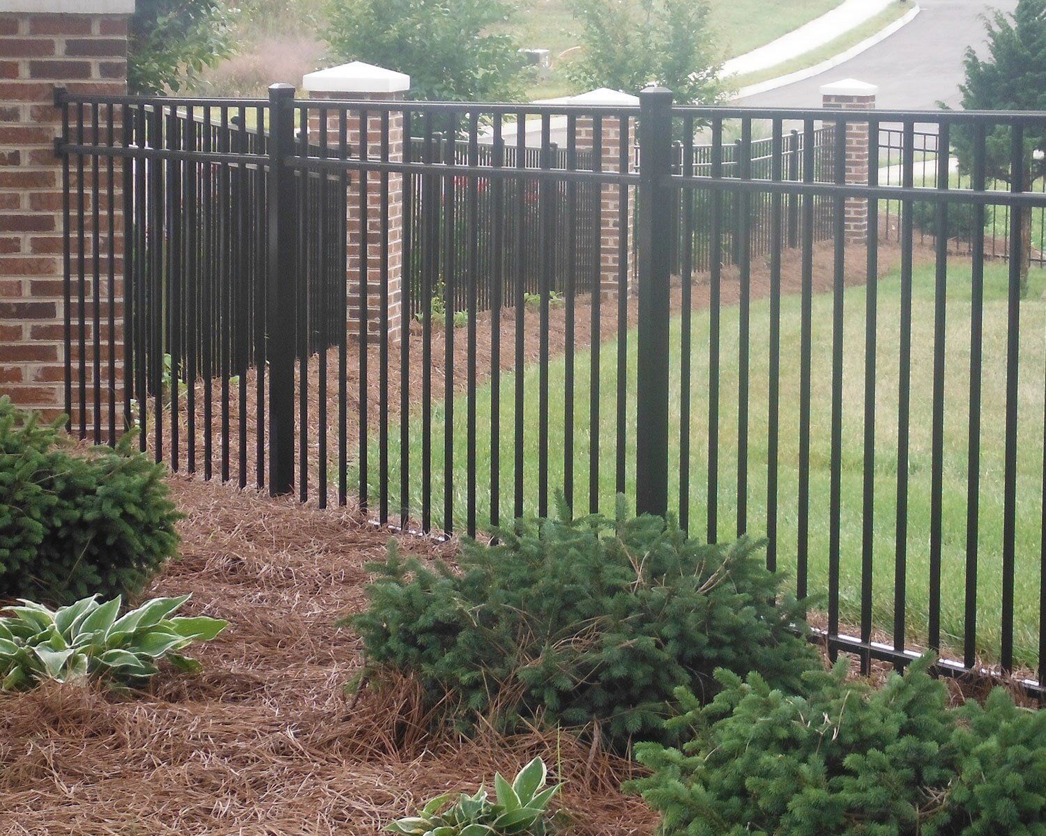 A black metal fence with a brick wall in the background