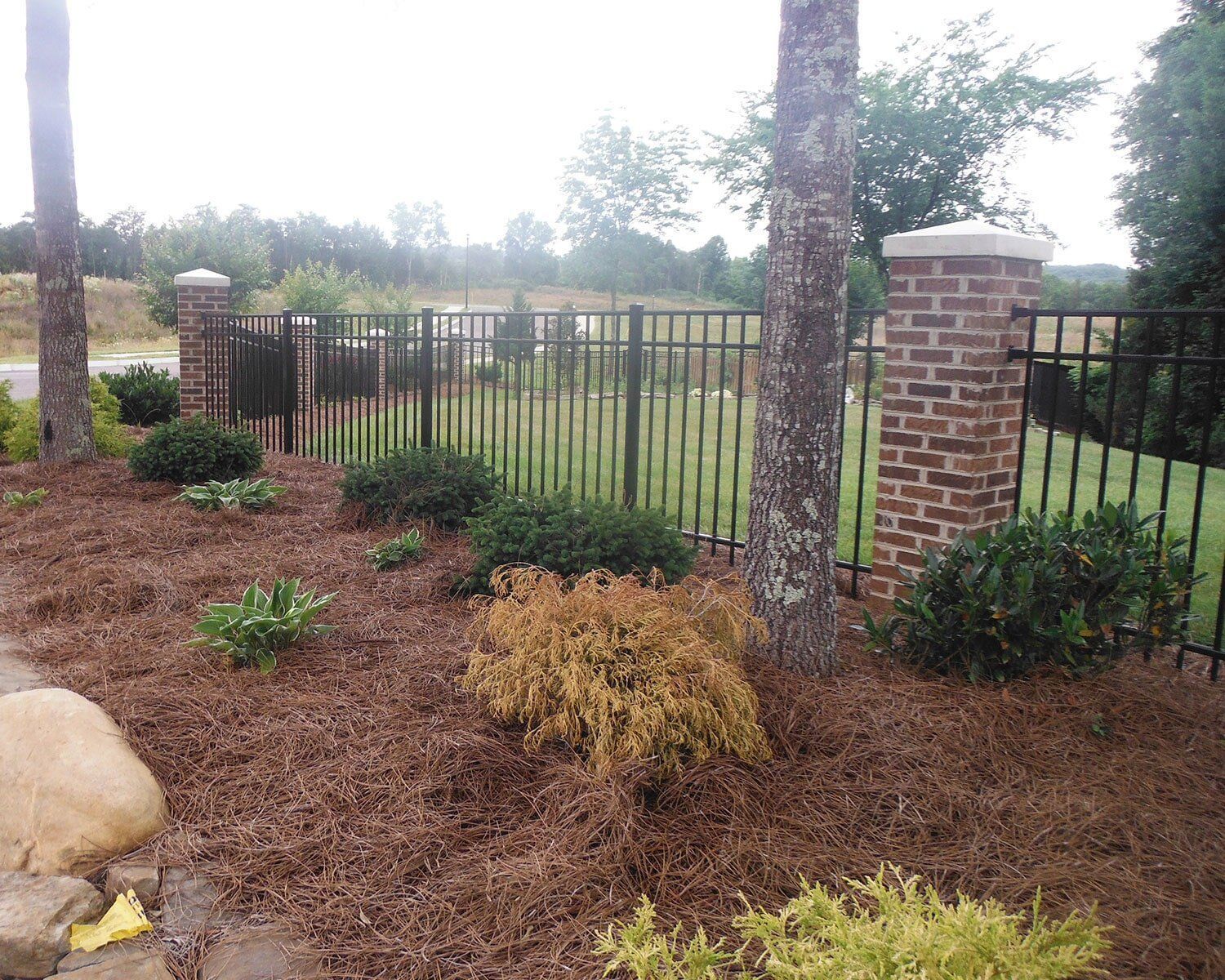 A metal fence surrounds a brick pillar in a garden