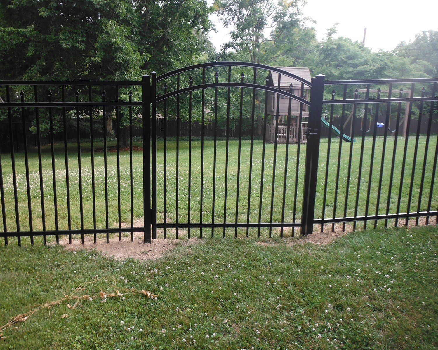 A black metal fence surrounds a lush green yard