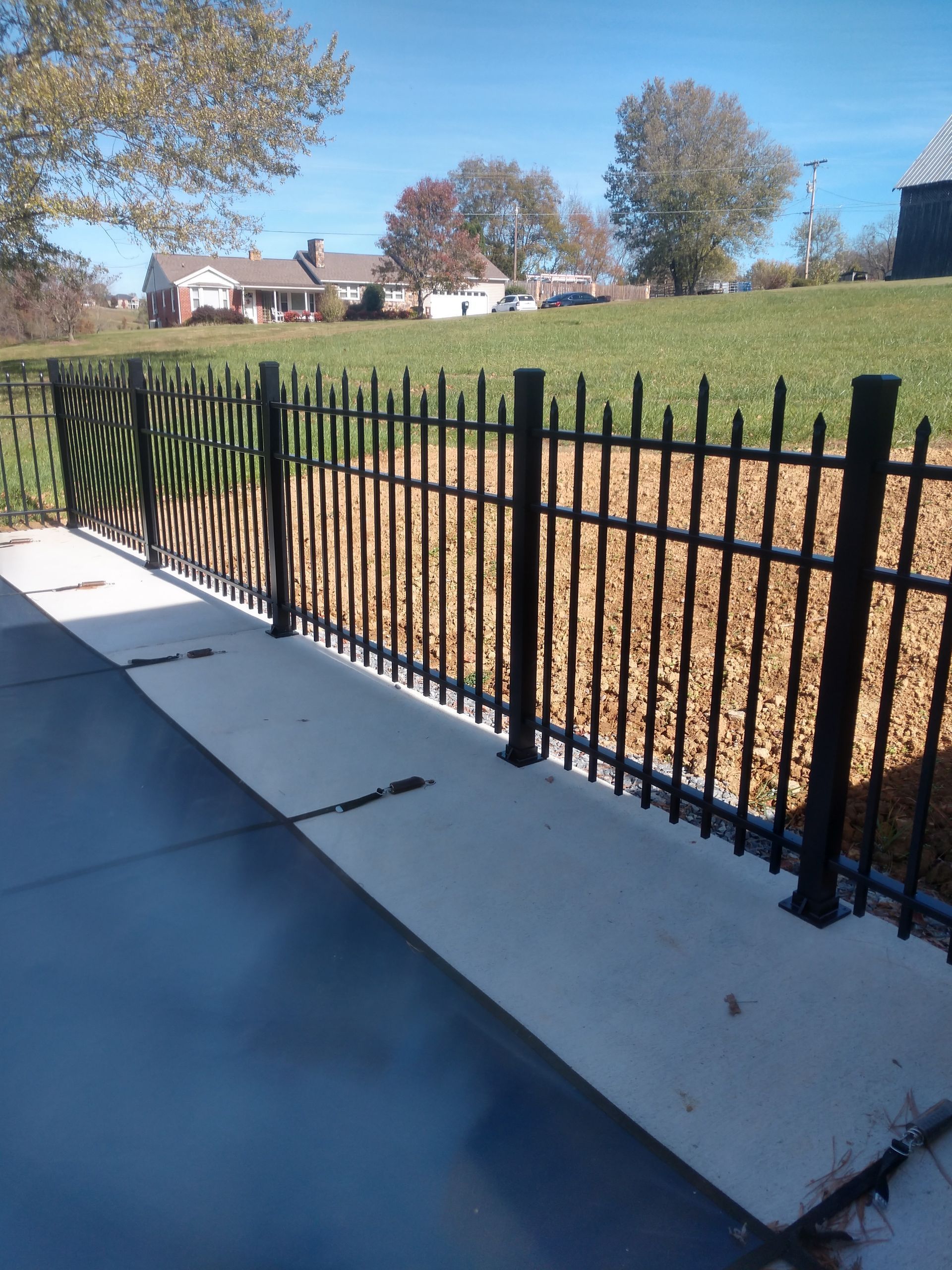 A black fence surrounds a concrete walkway with a house in the background