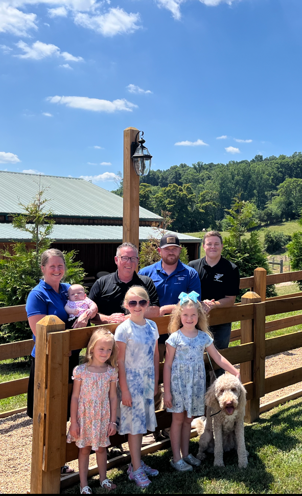 The Tri-City Fence family standing next to a wooden fence with a dog.