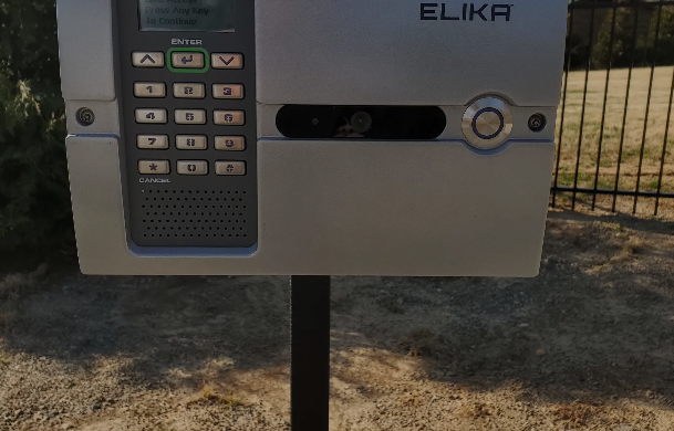 A keypad is sitting on top of a metal pole next to a fence.