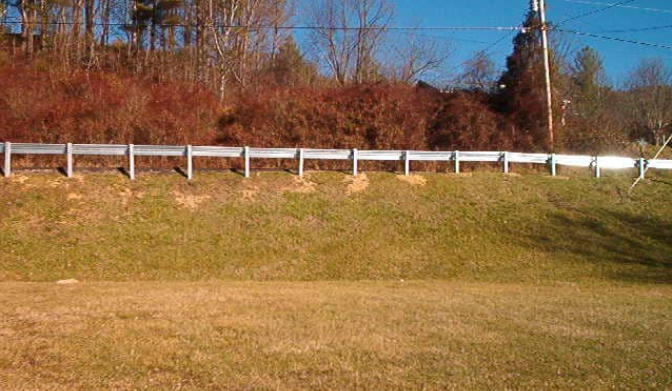A white fence surrounds a grassy hillside with trees in the background.