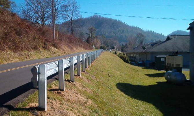 A road with a fence on the side of it and a house in the background.