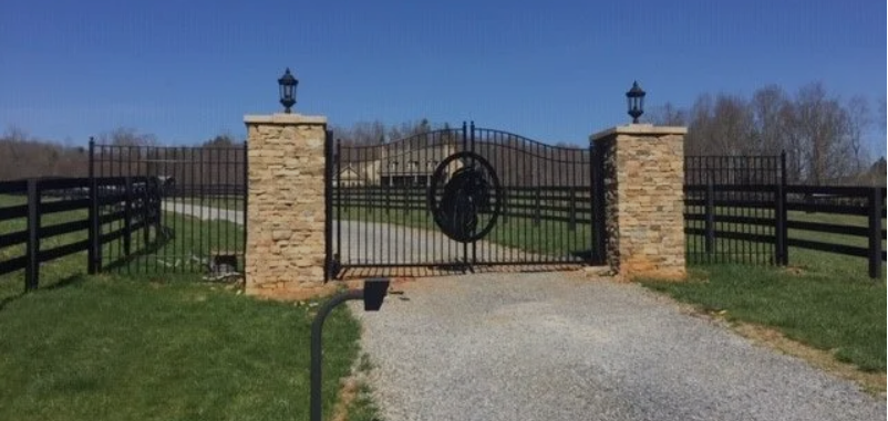 A metal gate with a horse on it is surrounded by a fence.