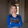 Une femme en salopette et chemise bleue sourit les bras croisés.