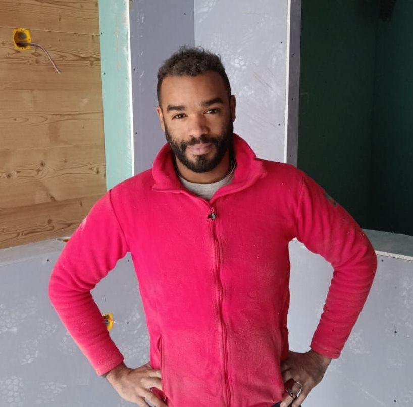 Un plombier est assis dans une salle de bain, tenant une clé et levant le pouce.