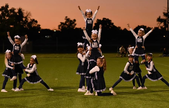 Cheerleader in red uniform performs a backbend on a green and red football field.