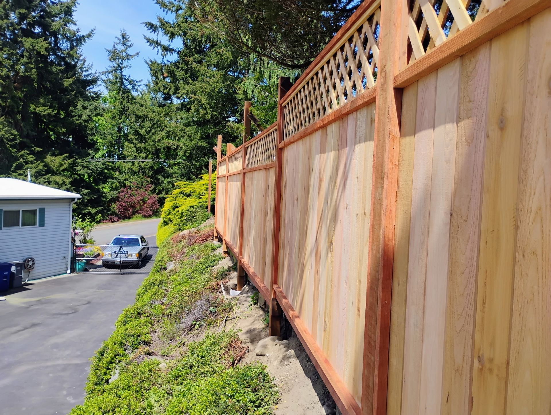 Wooden fence with lattice top along a driveway, with a house and trees in the background.