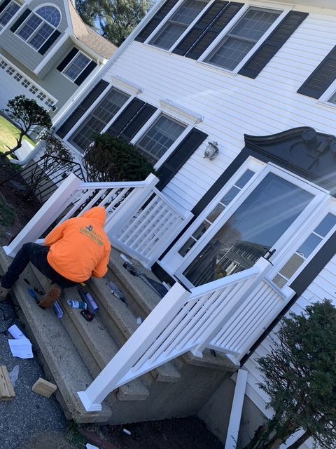 Person in orange jacket installing white handrails on concrete steps of a white house.