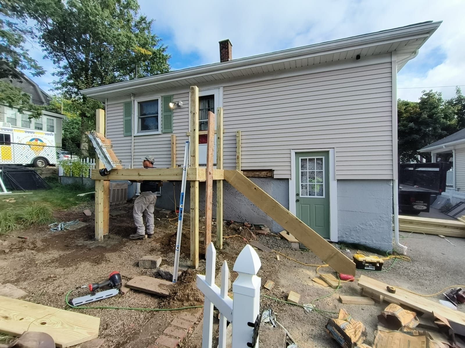Construction of a wooden deck with stairs attached to a house. A person works on the deck in front of the white house.